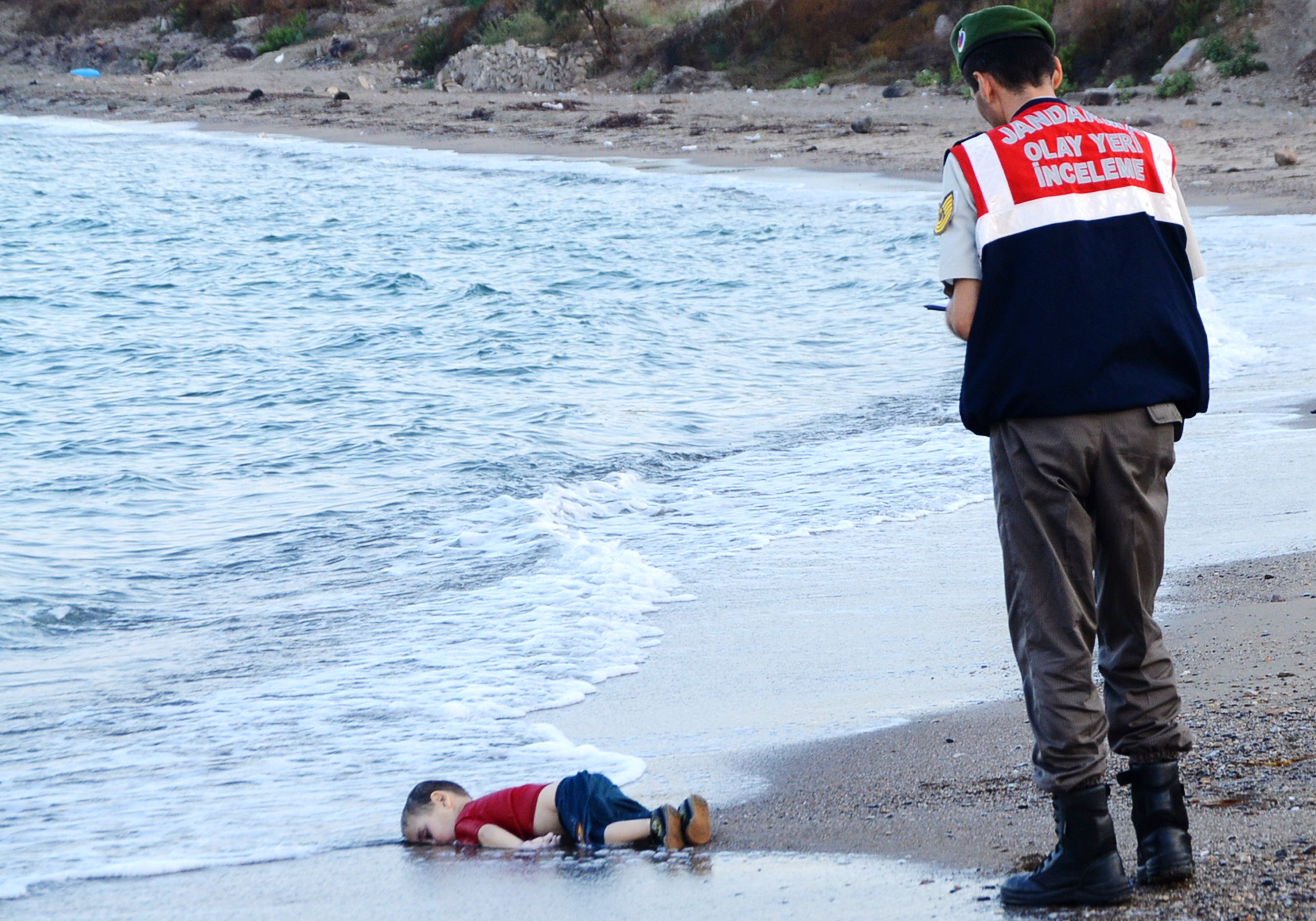 GRAPHIC CONTENT A Turkish police officer stands next to a migrant child's dead body off the shores in Bodrum, southern Turkey, on September 2, 2015 after a boat carrying refugees sank while reaching the Greek island of Kos. Thousands of refugees and migrants arrived in Athens on September 2, as Greek ministers held talks on the crisis, with Europe struggling to cope with the huge influx fleeing war and repression in the Middle East and Africa. AFP PHOTO / Nilufer Demir / DOGAN NEWS AGENCY = TURKEY OUT =